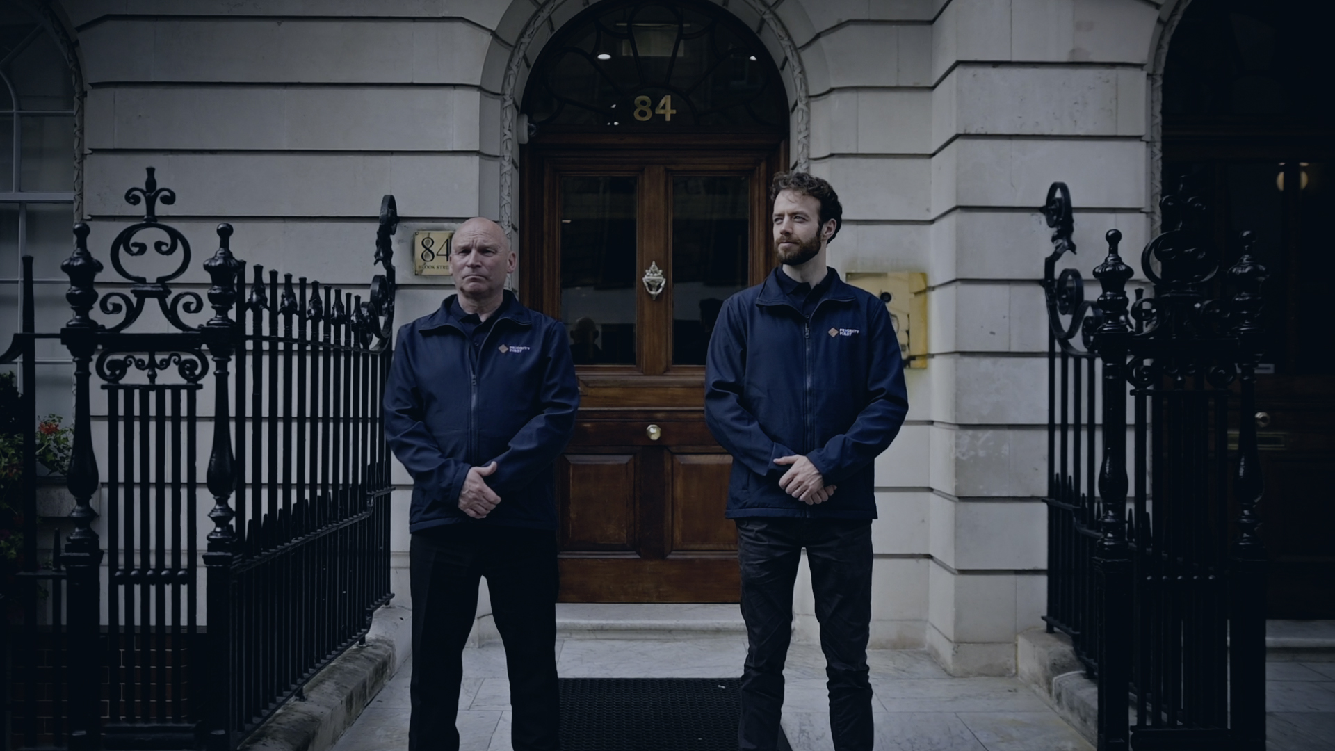 Two security officers on duty outside a London building at dusk
